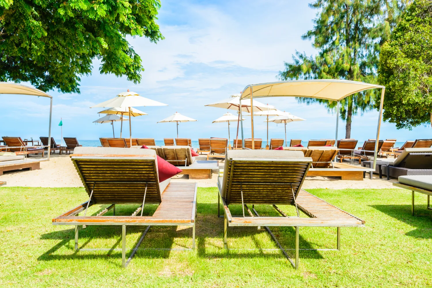 Sillas de playa en un entorno relajante junto al mar, con sombrillas y un paisaje verde, ideal para disfrutar del sol y la naturaleza.